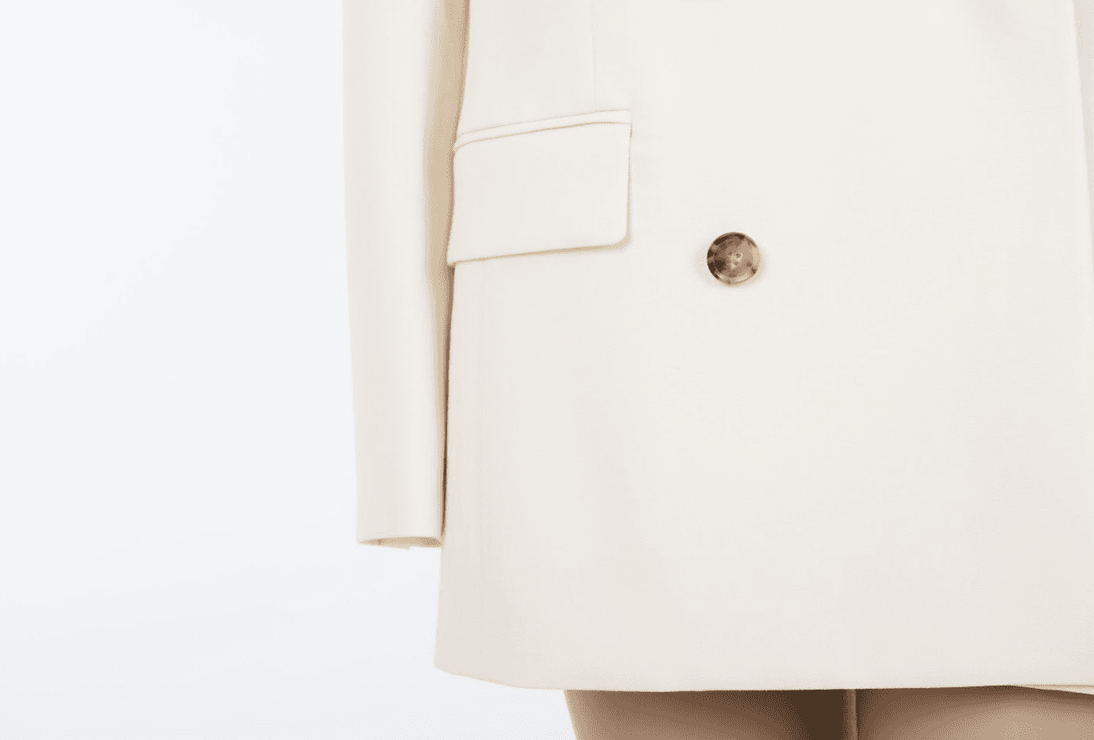 Macro detail of the FRAME Relaxed Double-Breasted Blazer showing the refined weave of the ivory fabric and the polished finish of the tortoise-style buttons.